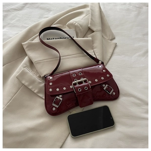 Detail of dark red patent leather shoulder bag with silver studs on beige suit