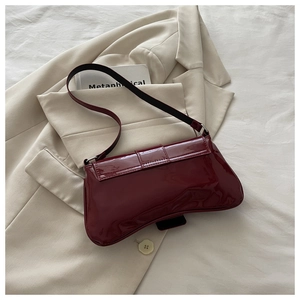 Detail view of burgundy patent leather underarm bag with unique curved base and glossy finish