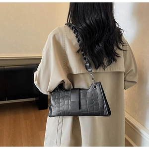 Detail of black croc-embossed baguette bag with unique braided shoulder strap texture