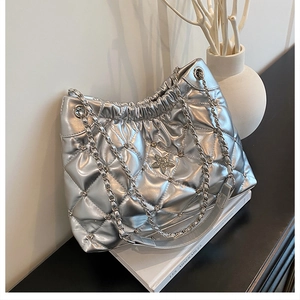 Close-up of silver quilted bucket bag with star badge, metal rivets and chain strap