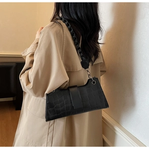 Detail of black crocodile texture baguette bag with thick braided shoulder strap on model