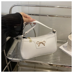 Close-up of white lychee texture leather underarm bag with gold bow and floral pendant