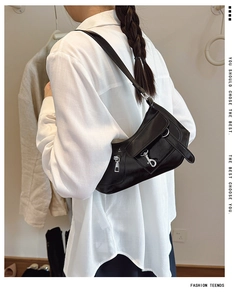 Close-up of glossy black underarm bag with silver buckle on model in white shirt