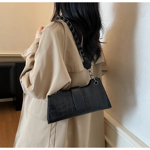 Close-up of black crocodile texture shoulder bag with chain strap worn by a model