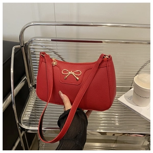 Detail of red pebbled leather baguette bag with golden bow and floral zipper pull