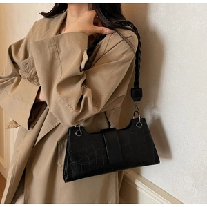 Detail of black crocodile texture shoulder bag with wide braided strap and silver ring