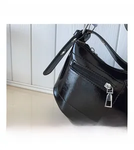 Close-up of shiny black patent leather underarm bag with silver zipper and eyelet strap