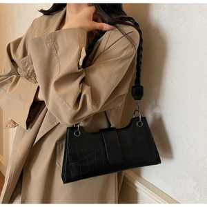 Detail of black crocodile texture baguette bag with a stylish woven shoulder strap