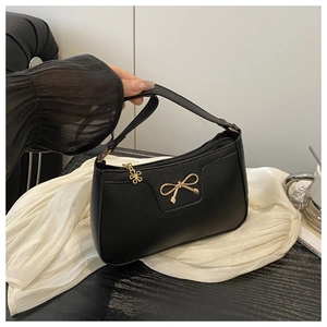Close-up of black lychee grain leather handbag with gold bow and flower pendant charm