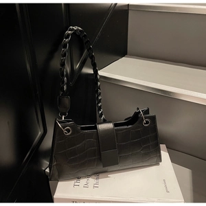 Close-up of black crocodile pattern baguette bag with stylish twisted woven strap