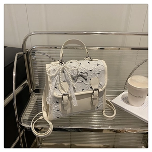 Détail d'un sac à dos en dentelle blanc crème avec nœuds et pendentif perle élégant