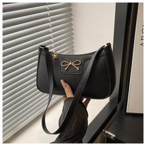Close-up of black pebbled leather baguette bag with golden bow and floral zipper charm