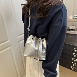 Silver metallic bucket bag with pearl chain and drawstring, shown cross-body on a model