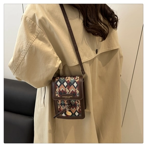 Detail view of retro geometric jacquard phone bag with brown leather trim on a model