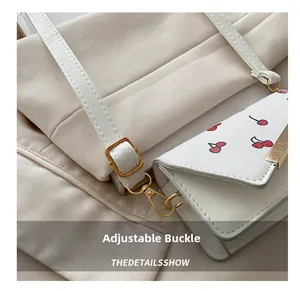 Detail of adjustable gold buckle and leather strap on white cherry print mini crossbody bag