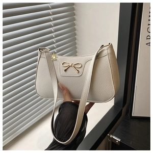 Detail of white lychee leather texture and golden bow buckle on underarm baguette bag