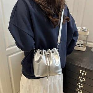 Silver metallic bucket bag with chain pearl detail shown on model in indoor setting