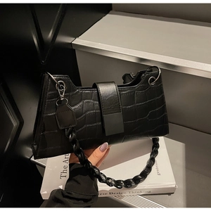 Close-up of black crocodile pattern bag with chunky braided strap and silver metal ring buckle