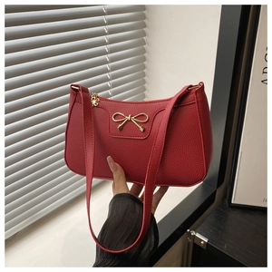 Detail of red PU leather underarm bag featuring a golden bow and butterfly zipper charm
