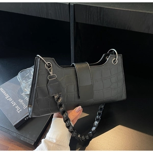 Detail of black crocodile pattern faux leather baguette bag with braided shoulder strap