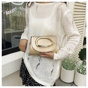 Close-up of champagne gold shoulder bag with oval buckle on a floral skirt background