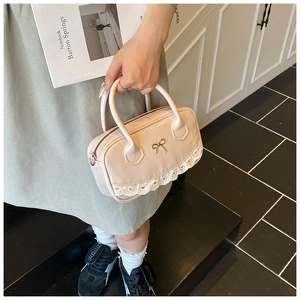 Detail of cream patent leather Boston bag featuring lace trim and gold bow accent
