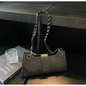 Detail of black crocodile pattern leather bag with braided handle on a bookshelf