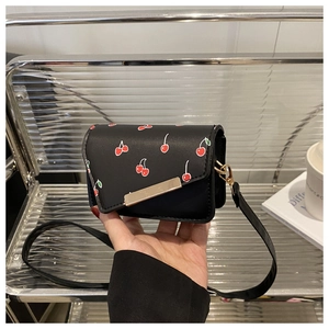 Close-up of a small black cherry print crossbody bag with a gold metal clasp and thin strap
