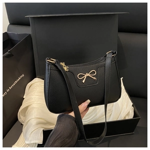 Detail of black pebbled leather handbag featuring a gold bow accent and zip pendant