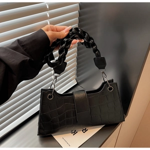 Close-up of black crocodile embossed texture and braided strap on shoulder bag
