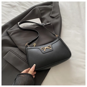 Close-up of black lychee grain leather bag with a golden bow metal accessory detail