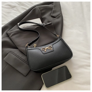Detail of black pebbled leather baguette bag with golden bow and flower pendant