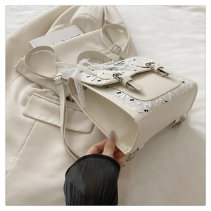 Détail d'un sac à dos crème avec broderie nœud, bords en dentelle et chaîne de perles