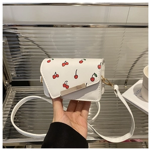 Detail of white PU leather crossbody bag with red cherry patterns and gold metal bar