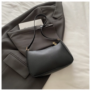 Detail of black pebbled leather baguette bag with clover-shaped gold zipper pendant