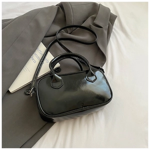 Dettaglio borsa Boston in vernice nera lucida su blazer grigio e lenzuola bianche