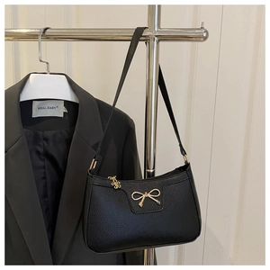 Detail of black lychee leather baguette bag with gold bow buckle and flower charm