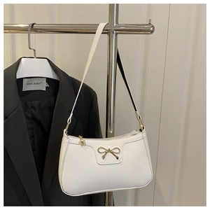 Detail of white lychee leather texture and golden metal bow on underarm bag