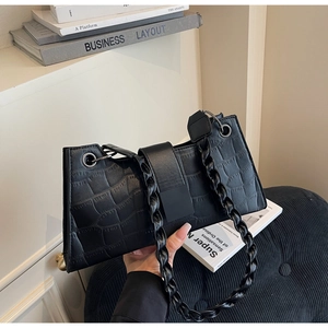 Close-up of black crocodile texture bag with woven strap and magnetic buckle detail