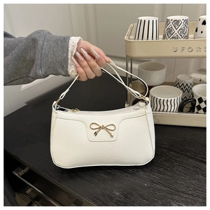 Detail of white litchi pattern leather baguette bag with golden bow hardware