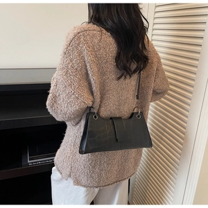 Detailed back view of a black crocodile-patterned baguette bag worn on a woman shoulder