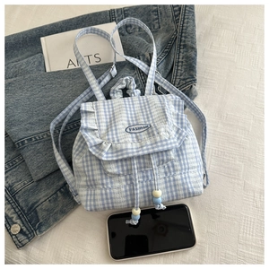 Detail of blue and white plaid backpack featuring ruffle trim and beaded drawstring closures