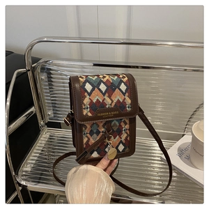Makroaufnahme von retro-geometrischem Jacquard-Stoff mit Goldanhänger an Ledertasche