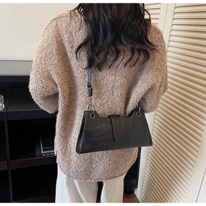 Detail of black crocodile pattern baguette bag worn on shoulder over a brown sweater