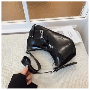 Detail of black glossy crescent bag showing chic zippers and polished leather texture
