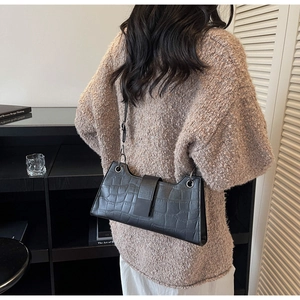 Detail showing crocodile embossed texture and metallic ring buckle on a black baguette bag