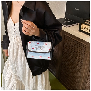 Detail of light blue handbag with red bow prints and a silver butterfly metal clasp