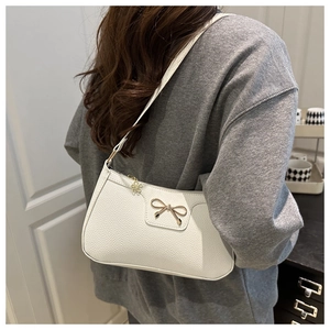 Close-up of white pebble leather baguette bag with gold bow and floral zipper charm