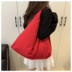 Detailed side view of a large red nylon tote bag on shoulder with soft pleated texture