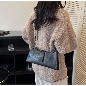Close-up of black crocodile pattern baguette bag with metallic ring and magnetic buckle